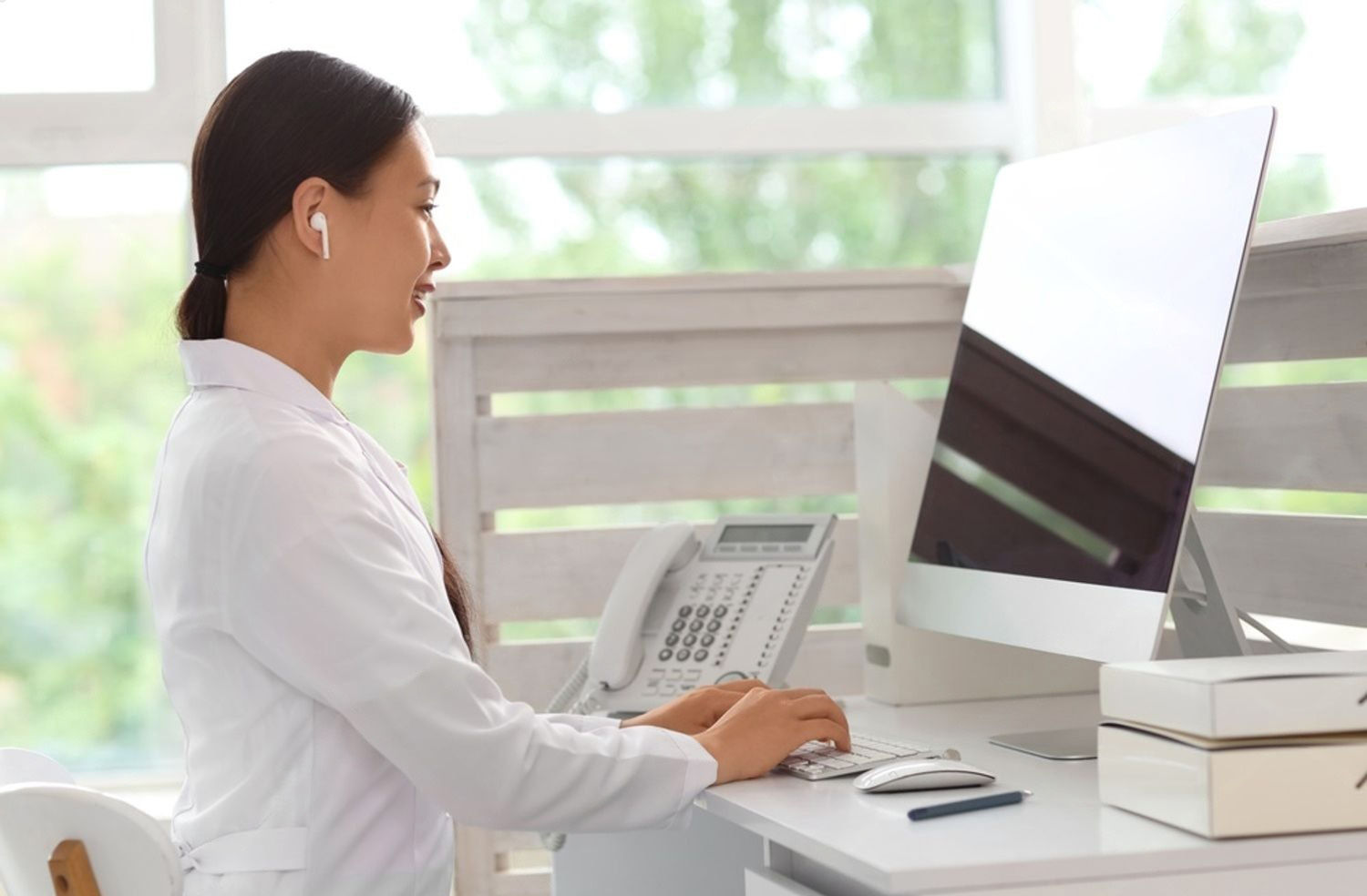 Recepcionista de clínica com fone de ouvido trabalhando no computador