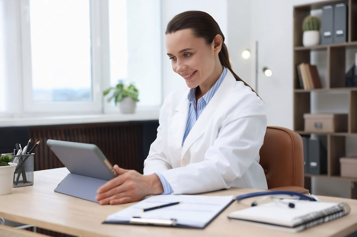 Profissional de jaleco sorrindo em frente a um tablet sobre a mesa
