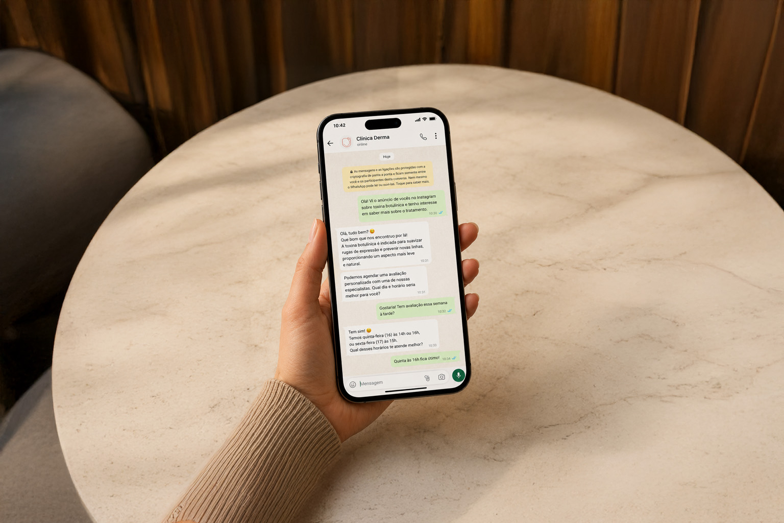 Mão segurando um celular com uma conversa de WhatsApp de clínica na tela